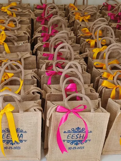 A large order of our bespoke jute bags, personalized with the bride's name and wedding date. The vibrant pink and yellow ribbons add a festive touch.