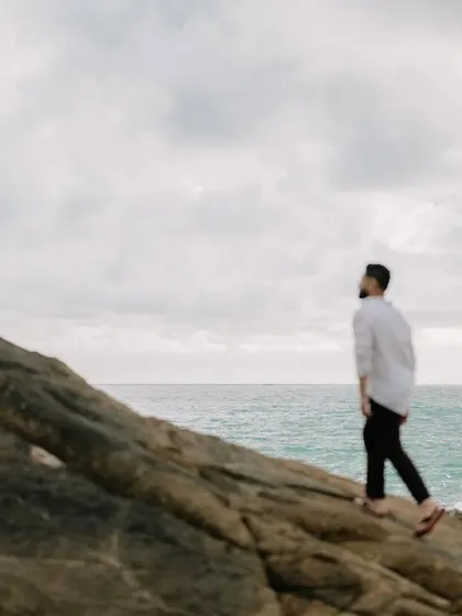 A solo shot of Harman walking along the rocky shoreline, creating a thoughtful and cinematic portrait.