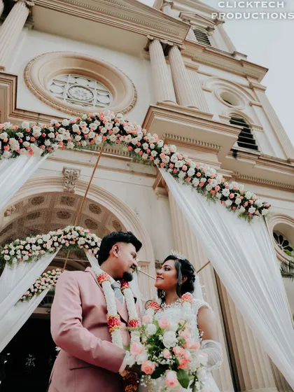A low-angle shot of the couple looking at each other, framed by the floral wedding arch at the church entrance.