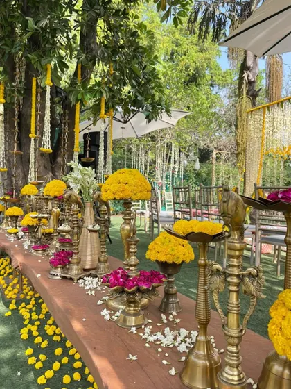 A close-up of a traditional Haldi decor setup, featuring brass vessels filled with vibrant marigolds and rose petals.