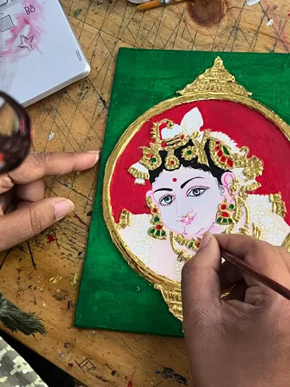 A student adds the final facial details to a small Tanjore portrait. This is the most delicate part of the process, requiring intense focus and a fine-tipped brush.