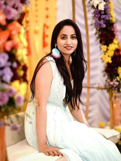 A guest poses at the Mehendi ceremony. The decor includes a swing decorated with colorful flowers, which is a popular spot for photos.