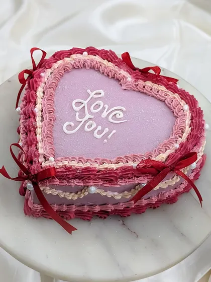 The details matter. This angle shows the delicate red ribbons and edible pearls that we add to our vintage heart cakes to give them an extra touch of elegance.