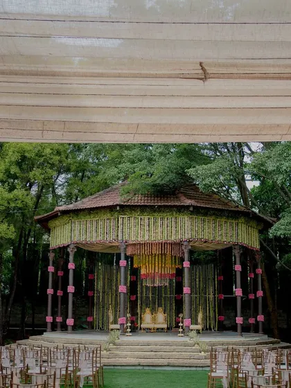 A wide view of the wedding setup, featuring a stunning mandap with a lotus-themed floral chandelier. The seating arrangement around the venue's fountain creates a picturesque and grand setting for the celebration.