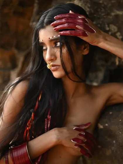 A creative editorial look featuring long, flowing hair with red thread accents and a dramatic reverse cat-eye. The makeup includes intricate dot work along the browline for a tribal-inspired aesthetic.