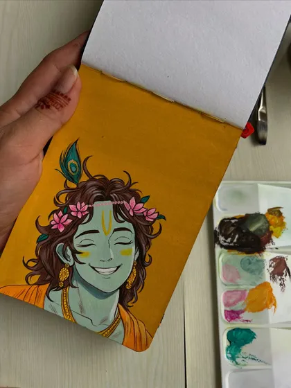 Holding the sketchbook with the Krishna painting, showing the scale of the artwork.