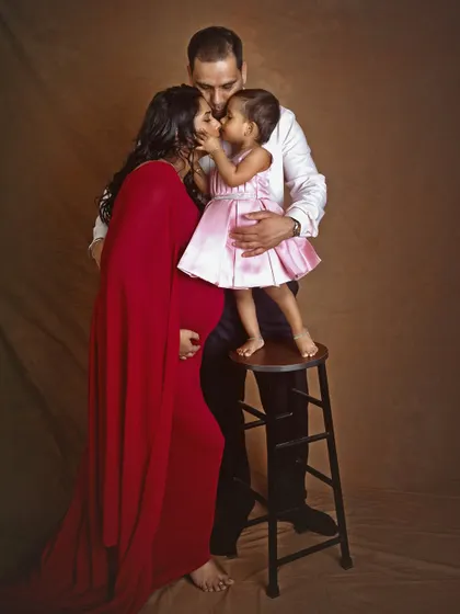 A heartwarming family portrait where a little girl stands on a stool to give her mother a kiss, while her father kisses her head. This image is a beautiful capture of family love during a maternity session.