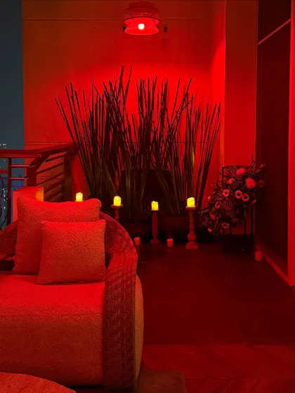 We use lighting to create mood. Here, a balcony seating area is bathed in dramatic red light, with tall plants and candles adding to the intimate, lounge-like feel.