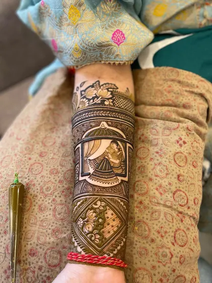 A full view of an arm design featuring a bride looking out from a jharokha. The central portrait is surrounded by detailed floral and geometric patterns.