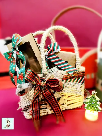 A rustic jute basket filled with sweets and treats for Christmas. The plaid bow and festive ribbons give it a classic holiday feel.