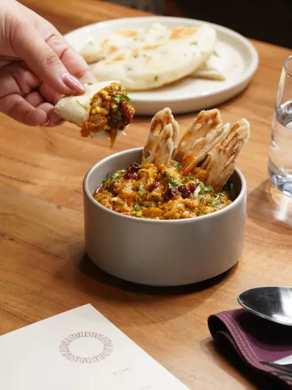 A shot capturing a person enjoying a flavorful bowl of baingan bharta with crispy naan, emphasizing the interactive experience of dining.