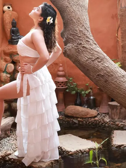 A full-length side profile of the Apsara outfit. This shot showcases the layered ruffles of the skirt and the model's graceful posture against the earthy backdrop.