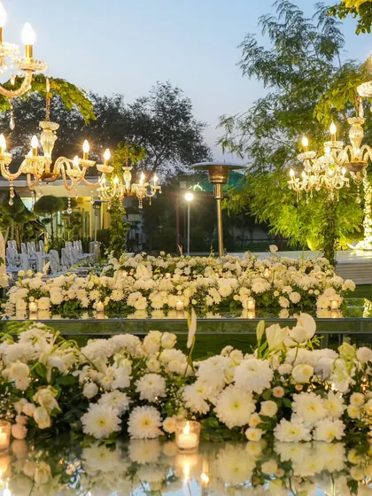 A table covered in a sea of white chrysanthemums and candles, with its mirrored surface reflecting the chandeliers and sky, creating an infinitely beautiful and romantic scene.