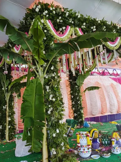 A traditional mandap setup for a puja, with pillars covered in greenery and banana plants.