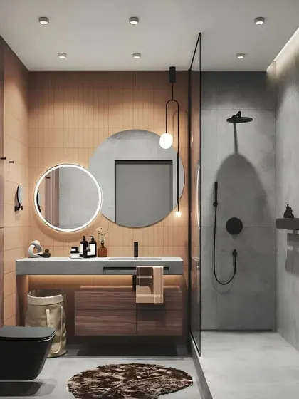 A modern bathroom with a mix of soft pink and grey tiles. The round back-lit mirror and hanging pendant light add a touch of elegance and create a soft, flattering glow.