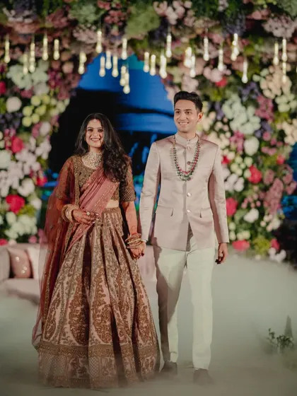The grand entrance. The couple walks in hand-in-hand at their reception, surrounded by theatrical smoke. Their coordinated outfits look stunning against the floral backdrop, creating a truly cinematic moment.