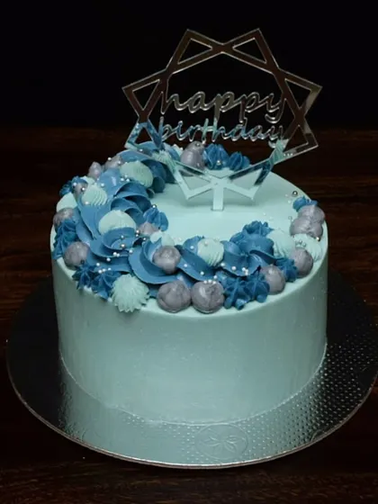 A pretty and elegant cake made with zero fondant. The light blue buttercream is decorated with a crescent of intricately piped swirls and rosettes in shades of blue and grey, topped with a modern acrylic topper.