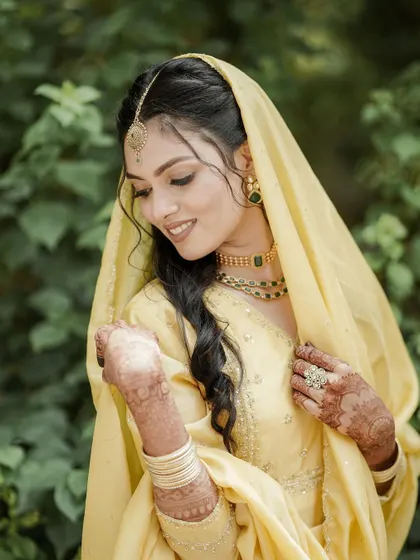 The bride looks down with a gentle smile, her hands adorned with henna, in this soft and beautiful portrait.
