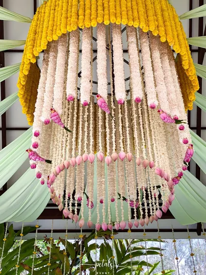 A close-up of the magnificent floral chandelier. It is crafted from marigolds, tuberoses, and lotus buds, with whimsical pink birds nestled among the flowers.