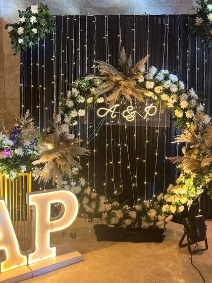 A personalized photo booth for a Sangeet. This setup features a floral ring against a dark backdrop with fairy lights, complete with illuminated initials of the couple.