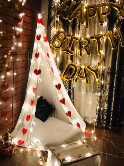 An indoor cabana tent setup for a birthday, decorated with fairy lights and heart cutouts, creating a perfect little hideaway for a romantic celebration.