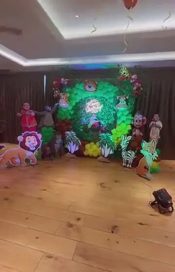 A wide shot of a jungle-themed party hall. The main backdrop is a dense arrangement of green balloons and foliage with various animal cutouts.