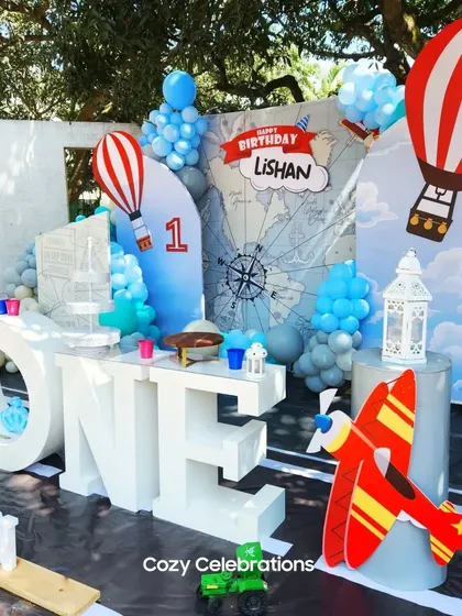An "Up and Away" travel and hot air balloon theme for a first birthday. The decor features a world map backdrop, airplane props, and cute hot air balloon details.