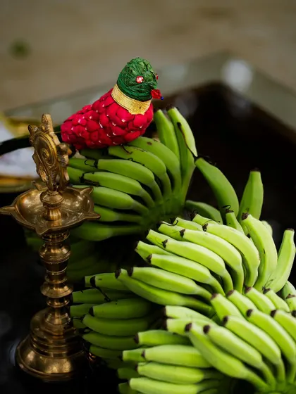 A detail from our styling workshop, showcasing a traditional brass lamp and a parrot crafted from cloth and beads, resting on a bunch of green bananas. It's all about finding beauty in unexpected combinations.