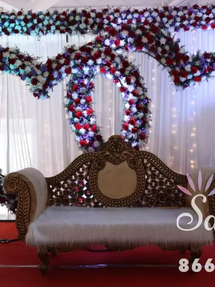 A romantic stage for an engagement or reception, featuring two interlocking hearts made of red and white flowers. The elegant sofa and simple lighting keep the focus on the beautiful floral centerpiece.