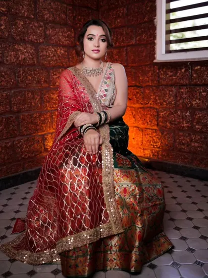 A seated portrait of a model in a stunning multi-colored lehenga. The warm lighting and the brick wall background give the photo a rustic and elegant feel.