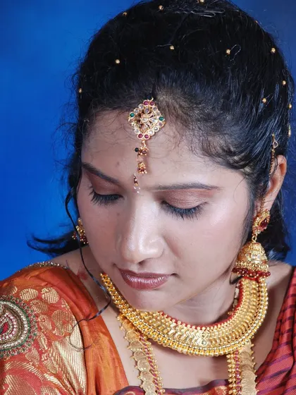 A serene, eyes-closed portrait of a bride, highlighting her makeup and heavy gold necklace.