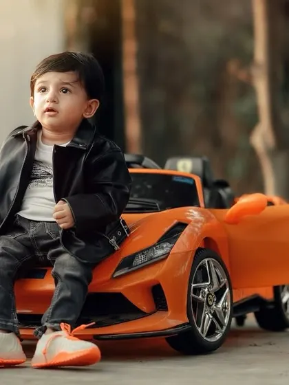 This little guy looks like a future movie star, posing coolly on his orange sports car. The leather jacket completes the look for this fun and stylish outdoor shoot.
