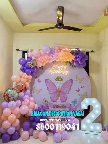 A beautiful butterfly theme for a 2nd birthday. The round backdrop is adorned with a pastel balloon arch and a large marquee number '2'.