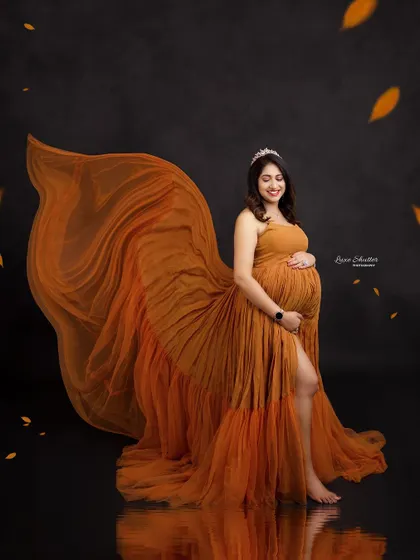 A stunning fabric toss with a mustard gown against a black backdrop. The falling leaves and water reflection create a dynamic and artistic autumn-themed portrait.