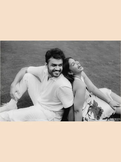 A joyful black and white portrait of the couple sitting back-to-back on the grass, sharing a laugh.