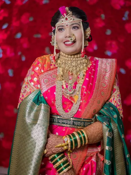 A stunning portrait of the bride in her vibrant pink and green wedding saree, adorned with heavy traditional gold jewelry.