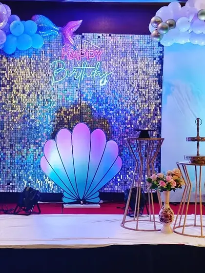 This mermaid stage combines a sequin backdrop with a large, iridescent seashell prop and a light-up number '5'. The color palette of blues, purples, and pinks creates a beautiful under-the-sea glow.