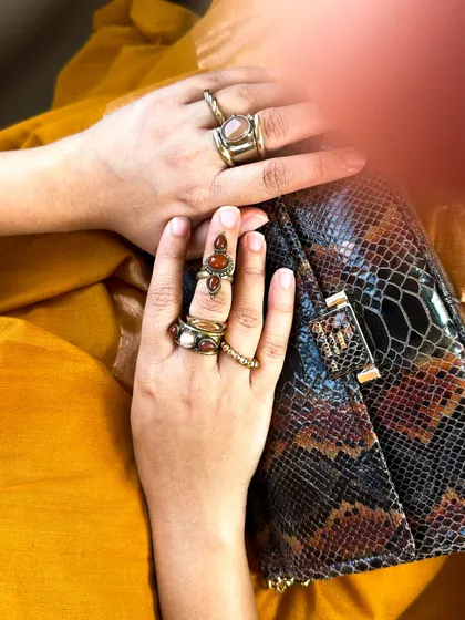 A detail shot of my hands, showing the stacked rings and the texture of the snakeskin clutch against the yellow khadi saree.
