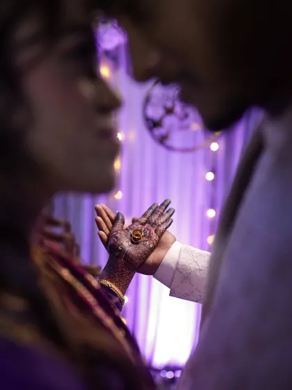 A unique perspective of the ring exchange, shot from behind the groom. The focus is on the ring resting in the bride's henna-covered palm, creating a sense of intimacy and anticipation.