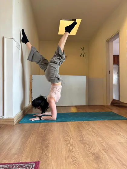 Forearm stand at the wall in a sunny corridor, hips stacked over shoulders.