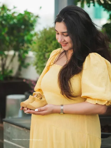 A smiling mother-to-be holds a pair of tiny baby shoes, a classic and heartwarming prop for any maternity photoshoot.