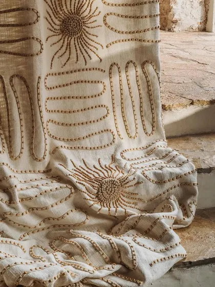Craftsmanship is at the heart of our collections. This close-up reveals the artistry of our 'Perpétuel Soleil' fabric, where each wooden bead is meticulously hand-embroidered onto a linen base to create a design that is both tactile and visually captivating.