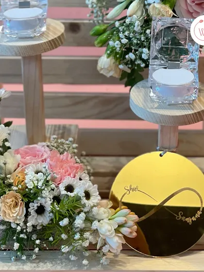 A close-up of a personalized ring platter. This design features a rustic two-tiered wooden stand, crystal ring holders, and a custom gold acrylic tag with the couple's names entwined in an infinity symbol.
