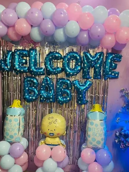 A "Welcome Baby" boy decoration with a blue foil curtain backdrop. The setup includes balloon pillars and a baby-themed foil balloon.