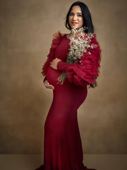 A full length portrait where the soft, glowing makeup complements the dramatic red dress perfectly. This is a classic maternity photoshoot look.