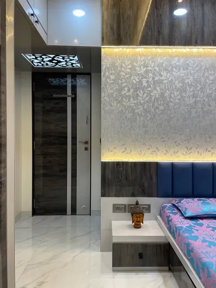 A detail shot of a bedroom, showing a backlit textured wallpaper panel above a blue upholstered headboard. The design uses layers of light and texture to create a visually rich and calming space.