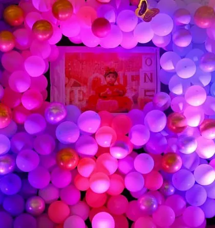A creative photo opportunity with a dense balloon wall in shades of pink and purple. The birthday girl is framed in the center for a unique first birthday picture.