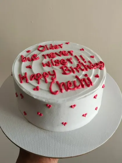 A cheeky "Older but never wiser" message on a minimalist cake with tiny hearts.