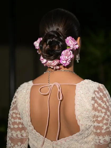 A detailed shot of the elegant bridal bun, adorned with fresh pink and white carnations. The hairstyle is a work of art.