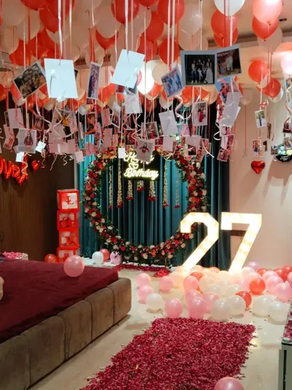 I can create romantic and surprising birthday decorations right in your bedroom. This setup features a floor-to-ceiling display of red and pink balloons, a path of rose petals, a custom floral and balloon ring, and photos hanging from the ceiling to celebrate precious memories.